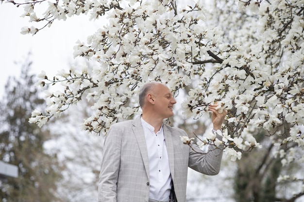 Mooie lachende man op de achtergrond van wit bloeiende magnolia