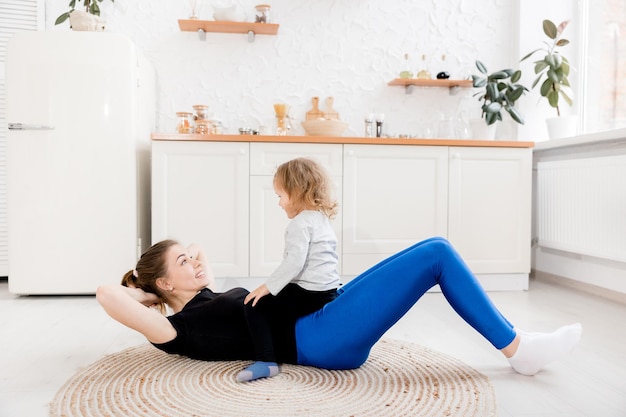 Mooie lachende moeder gaat 's ochtends sporten met haar dochtertje in de keuken Gezond levensstijlconcept Training tijdens quarantaine met een klein kind