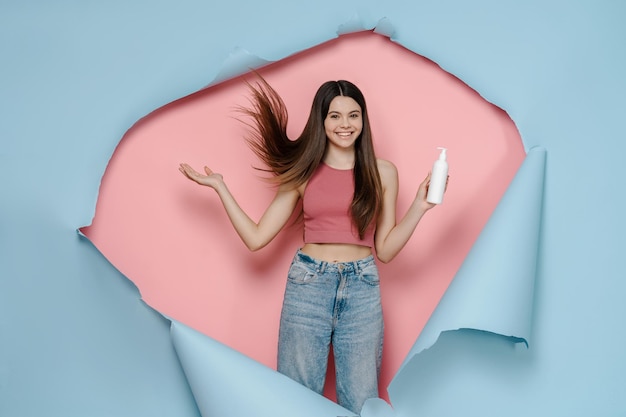 Mooie lachende tienermeisje met lang haar met shampoo geïsoleerd op blauwe roze achtergrond