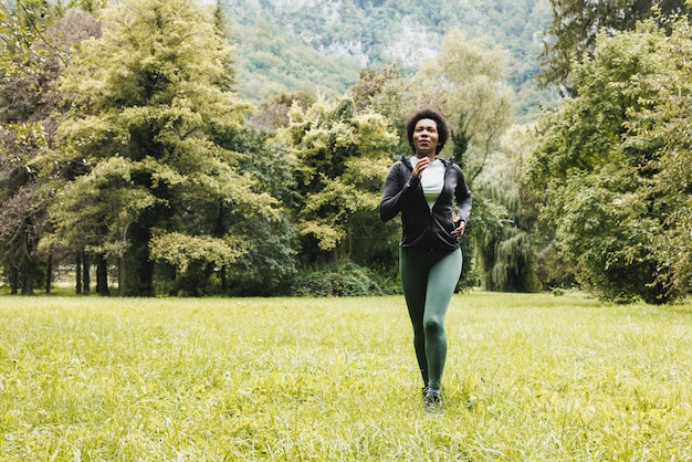 Mooie lachende volwassen Afro-Amerikaanse vrouw loopt door groen gras in de buurt van het berglandschap.