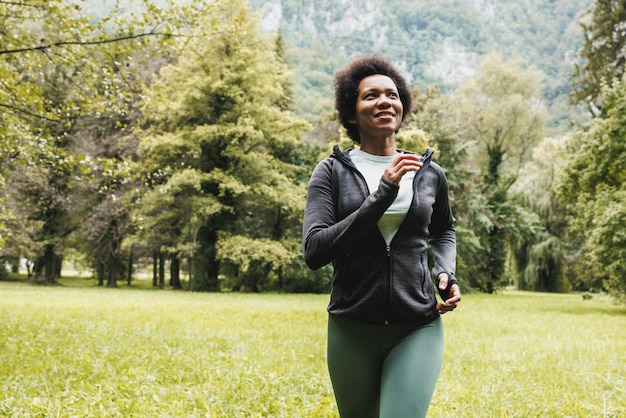 Mooie lachende volwassen Afro-Amerikaanse vrouw loopt door groen gras in de buurt van het berglandschap.