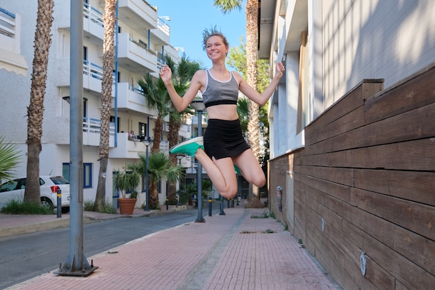 Mooie lachende vrolijke sport meisje tiener springen, vliegen in de lucht, kleine stad straat achtergrond. Actieve, atletische, gezonde levensstijl, jeugdtieners