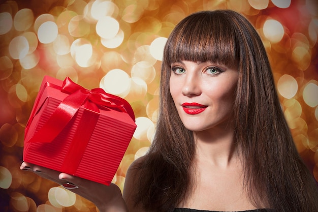 Mooie lachende vrouw, bruin steil lang haar met rode geschenkdoos, glanzende boke achtergrond