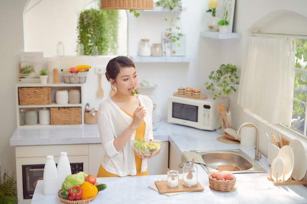 Mooie lachende vrouw die verse biologische vegetarische salade eet in moderne keuken.