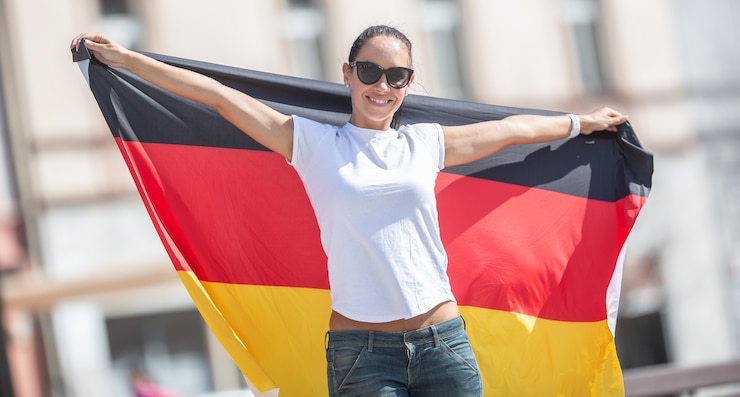 Foto mooie lachende vrouwelijke fan in zonnebril houdt een duitse vlag achter haar buitenshuis.