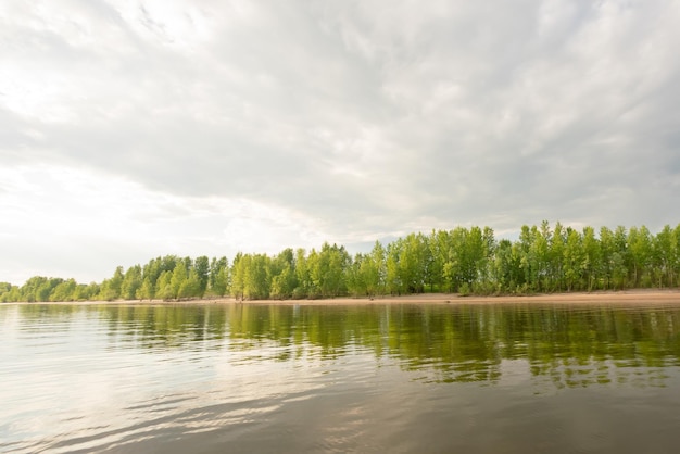 Mooie landschapsrivierhemel met wolken en zandstrand met groene bomen