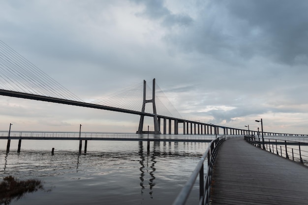 Mooie lange brug met een houten pier en de zee tegen een bewolkte hemel Vasco da Gama-brug in Lissabon
