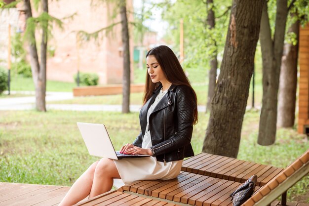 Mooie langharige vrouw, student werkt, communiceert, studeert met behulp van haar laptop buiten in het park in de zomer.