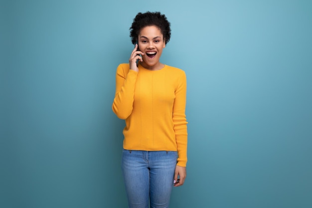 Mooie latijns-vrouw met afrohaar in casual gele blouse praten aan de telefoon