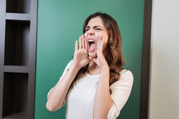 Mooie Latijnse vrouw die luid naar de andere kant schreeuwt met de hand op de mond. Communicatieconcept.