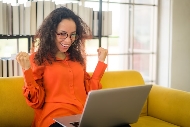 Mooie latijnse vrouw die met een laptop op de bank werkt met een gelukkig gevoel