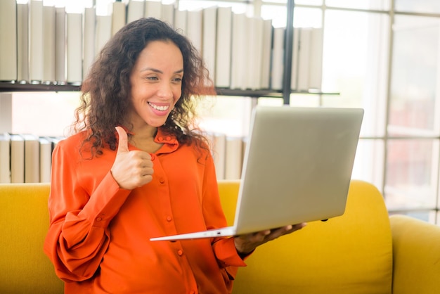 Mooie Latijnse vrouw die met een laptop op de bank werkt met een gelukkig gevoel