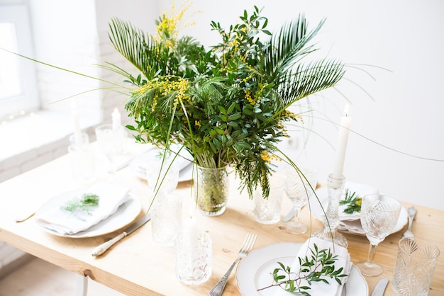 Mooie lentetafel met groene bladeren en mimosa-takken helder wit tafeldecor