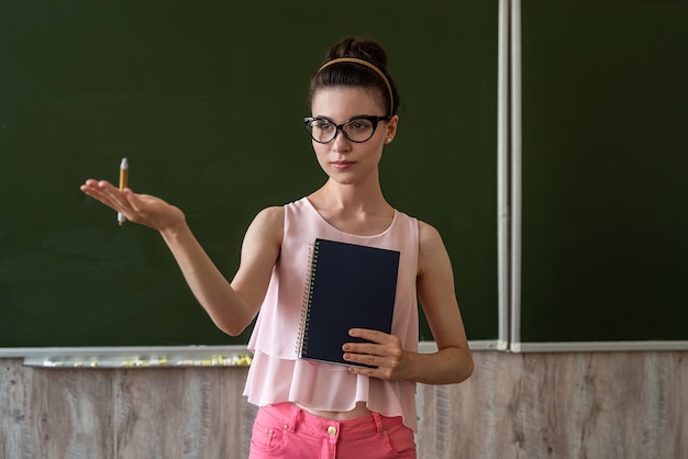 Mooie leraar legt nieuwe les uit in de buurt van het lege schoolbord, kopieer ruimte voor tekst