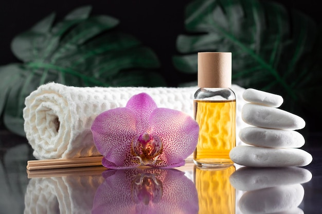 Mooie lila orchideebloem, heldere fles gele olie of parfum, houten stokjes en opgerolde handdoek