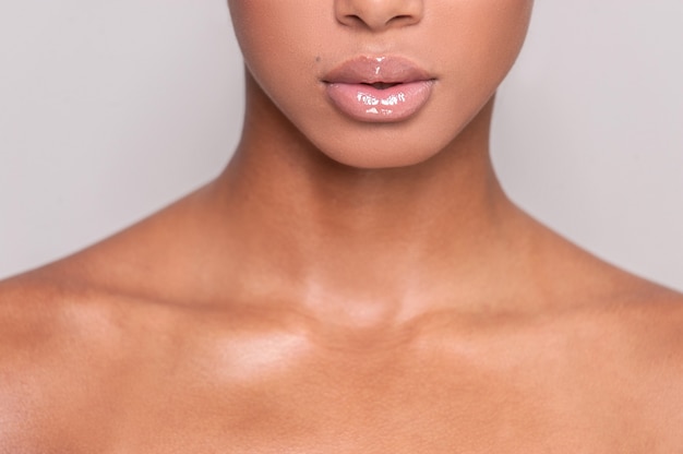 Mooie lippen. Bijgesneden afbeelding van mooie jonge Afro-Amerikaanse shirtless vrouw staande terwijl geïsoleerd op een grijze achtergrond