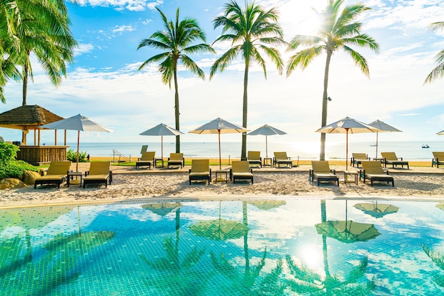 Mooie luxe parasol en stoel rond buitenzwembad in hotel en resort met kokos palmboom op blauwe hemel - concept vakantie en vakantie