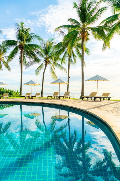 Mooie luxe parasol en stoel rond buitenzwembad in hotel en resort met kokospalm op zonsondergang of zonsopganghemel - vakantie- en vakantieconcept