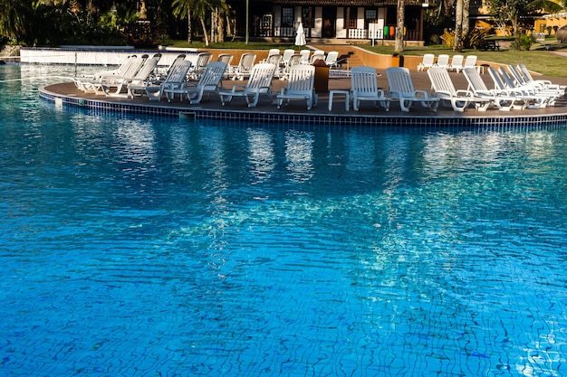 Mooie luxe parasol en stoel rond buitenzwembad in hotel en resort met kokospalm tegen blauwe hemel Strand op de achtergrond Reflecties in het water