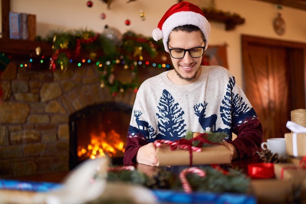 Mooie man in kerstmuts drinken geschenken maken Mooie achtergrond met open haard Gezellige plek