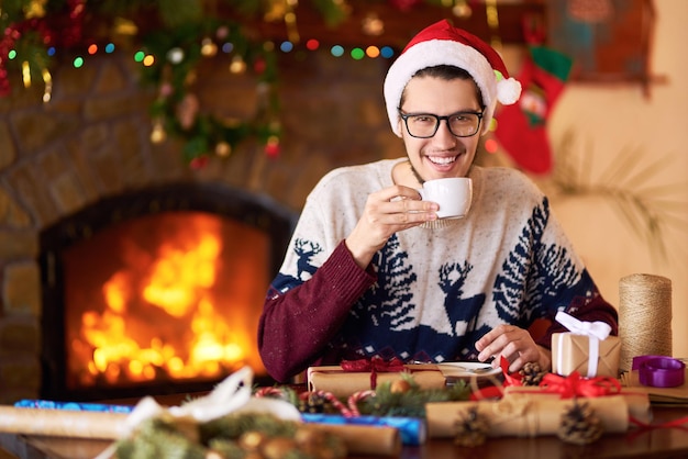 Mooie man in kerstmuts drinken geschenken maken Mooie achtergrond met open haard Gezellige plek