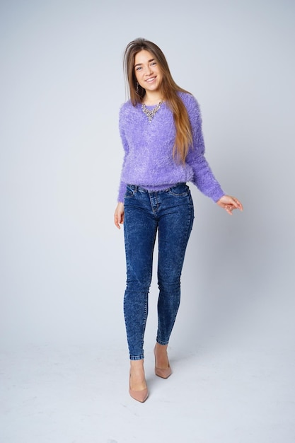 Mooie mannequin in paarse trui en jeans op grijze achtergrond