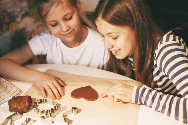 Mooie meisjes in de huiskeuken aan tafel snijden hartvormige koekjes uit het deeg