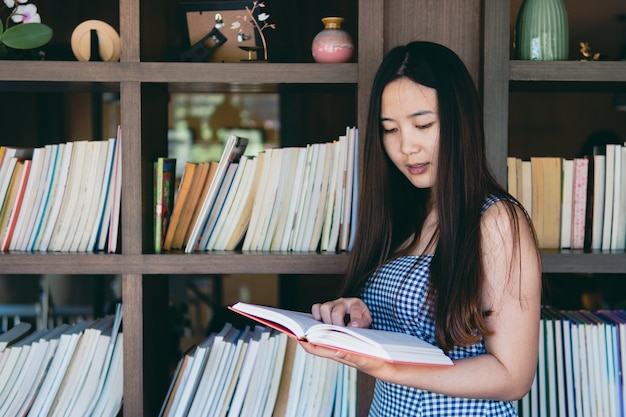 Mooie meisjes jonge vrouw die en zich tegen boekenplank bij bibliotheekruimte bevinden leunen