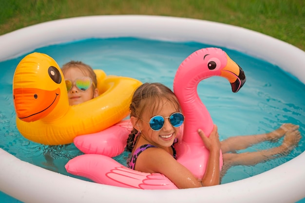 Mooie meisjes ontspannen thuis in een minizwembad dat spettert met opblaasbare cirkels
