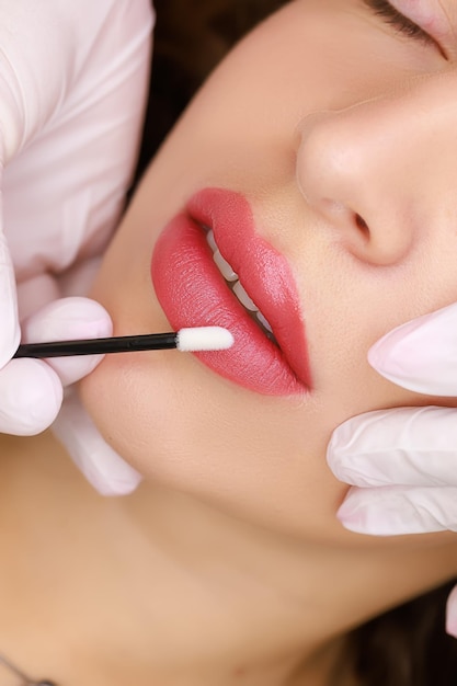 Mooie meisjes voerden de procedure uit van permanente lip make-up meester hydrateert de lippen met een borstel