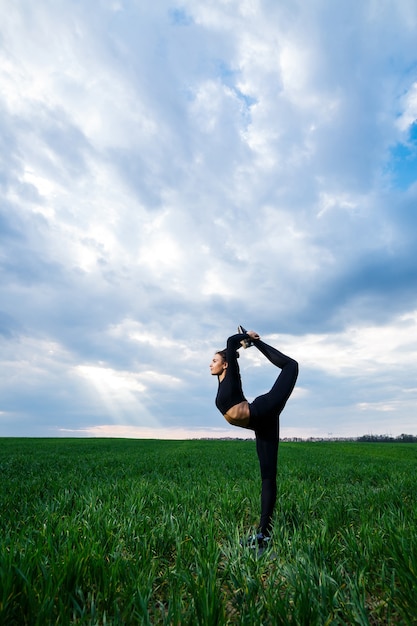 Mooie meisjesturner op het groene gras doet yoga. Een mooie jonge vrouw op een groen gazon voert acrobatische elementen uit. flexibele turnster in het zwart doet een handstand in split