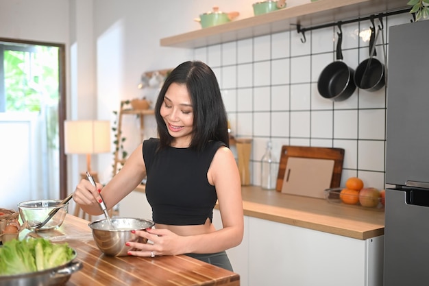 Mooie millennium vrouw koken gezonde maaltijd mengen ingrediënten in een schaal over de toonbank