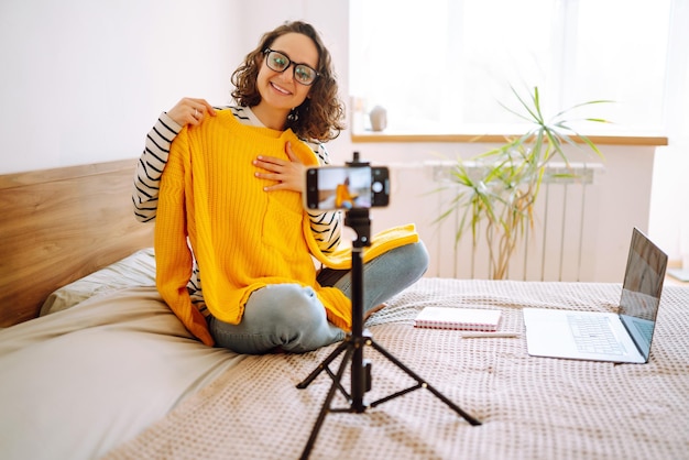 Mooie modeblogger die gele trui vasthoudt en dromerig video opneemt voor vlog Online marketing