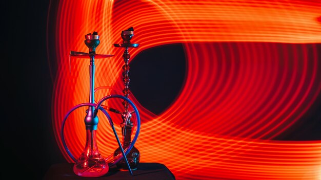 Mooie moderne waterpijpen met hete shisha-kolen in kommen op de tafel op een donkere achtergrond met rode neon gloed