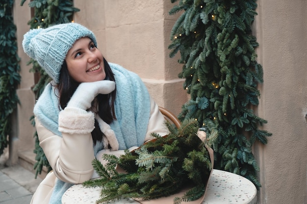 Mooie modieuze vrouw zittend op de stoel in openlucht café met kerstboom boeket