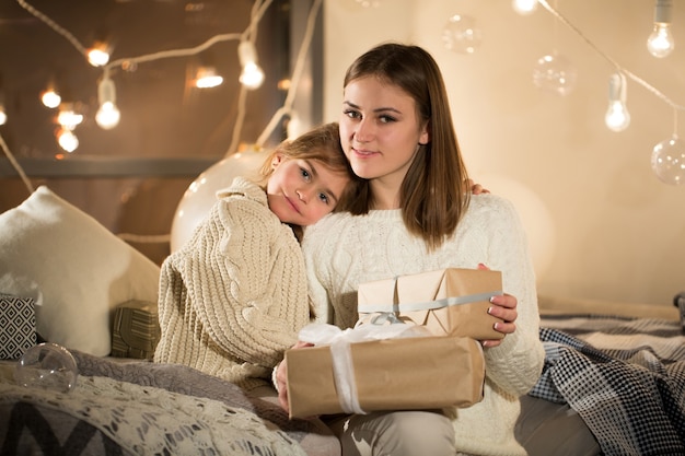 Mooie moeder en dochter openen een magisch kerstcadeau in het gezellige interieur van het huis. Nieuwjaar.