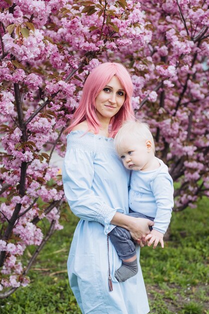 Mooie moeder houdt een kleine schattige zoon in haar armen, moeder en kleine babyjongen in een bloeiende tuin Sakura