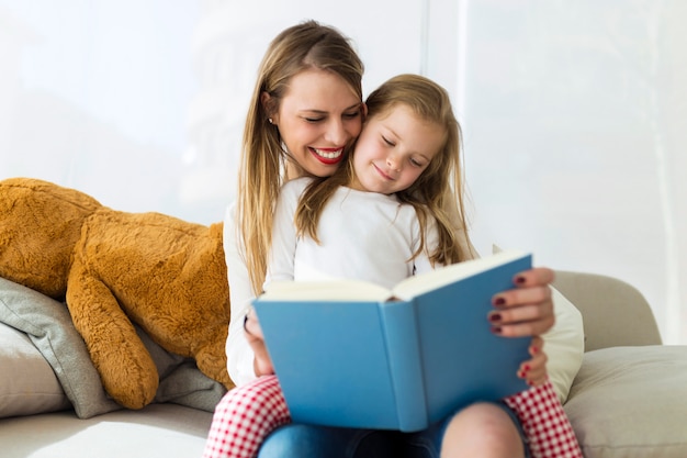 Mooie moeder met haar dochter die een boek thuis leest.