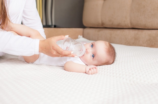 Mooie moeder voedt babymeisje uit een fles melk thuis.