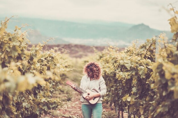 mooie mooie blanke vrouw loopt alleen in de wijngaard groene achtergrond zingen een ukelele akoestische gitaar