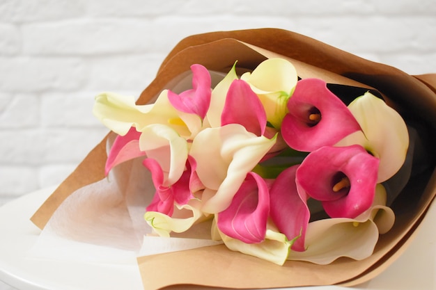 Mooie mooie callas in stijlvol kraftpapier op witte tafel.