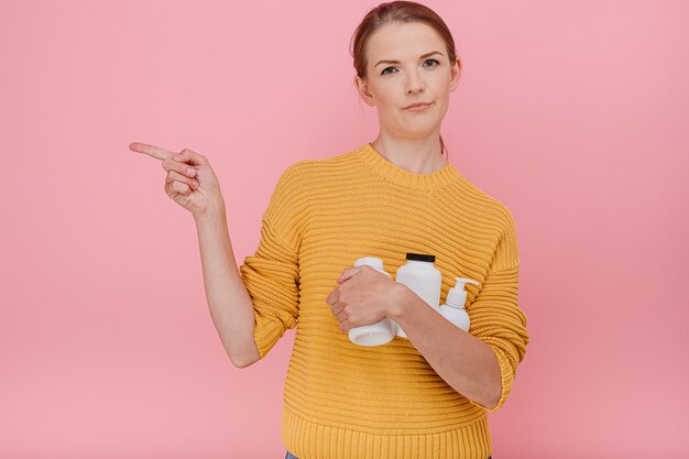 Mooie mooie vrouw met een fles medische pillen of vitamines die terloops gekleed is met een twijfelachtige uitdrukking