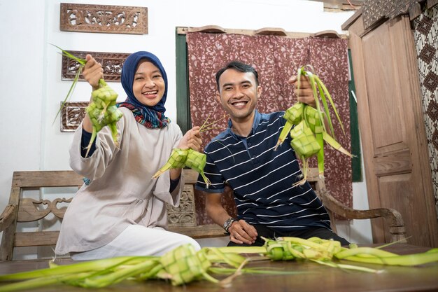 Mooie moslimfamilie en vriend die thuis ketupat-rijstwafel maakt met palmblad voor eid fitr mubarak-traditie