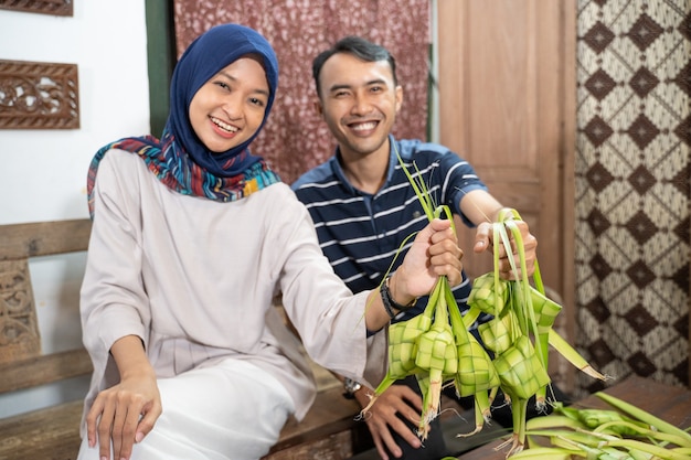 Mooie moslimfamilie en vriend die thuis ketupat-rijstwafel maakt met palmblad voor eid fitr mubarak-traditie