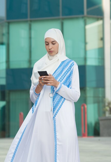 Mooie moslimvrouw die op een mobiele telefoon in openlucht texting.