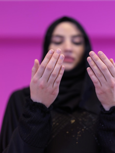 mooie moslimvrouw in modieuze jurk met hijab die traditioneel tot God bidt, houdt handen in biddend gebaar geïsoleerd op roze achtergrond die moderne islammode en ramadan kareem vertegenwoordigt