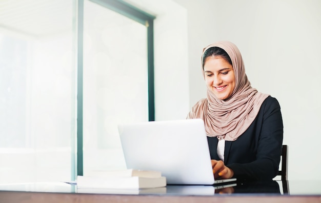 Mooie moslimvrouw met lichte huid in hijab die in de lichte kantoorruimte werkt