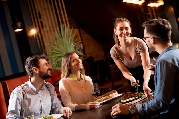 Mooie ober vrouw serveert groep vrienden met eten in de restaura