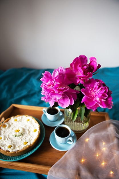 Mooie ochtend vanille cheesecake, koffie, blauwe kopjes, roze pioenrozen in een glazen vaas.