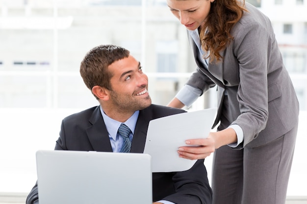 Mooie onderneemster die een document toont aan haar collega die aan laptop werkt